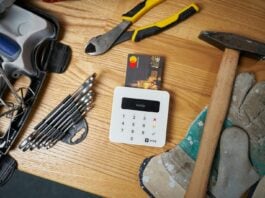 Construction payment - Overhead view of bright small plastic card in white contemporary wireless cash register surrounded by screwdriver set and hammer on big dirty gloves next to pliers